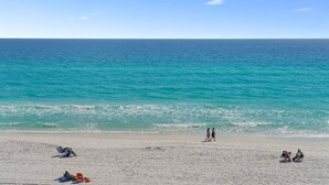 Une plage avec une eau turquoise et limpide, des gens qui se promènent et des chaises de plage.