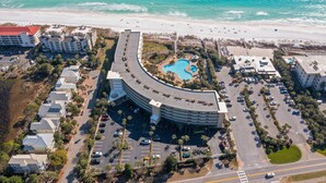 Vue aérienne d’un complexe hôtelier comprenant un bâtiment aux lignes courbes, une piscine et une plage.