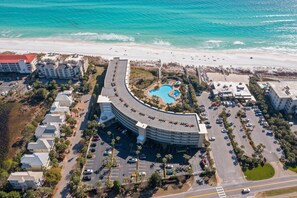 Vue aérienne d’un complexe hôtelier avec un bâtiment aux lignes courbes, une piscine et une plage.