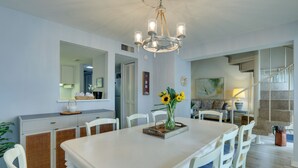 A dining area with a white table, white chairs, a chandelier, and a vase with sunflowers. - Pool & Beach Access: Hilton Head Island Villa! (Hilton Head Island)
