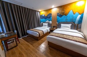 A hotel room with two beds, a wooden floor, a desk, and a curtain.