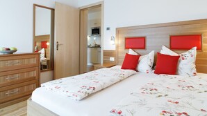 A hotel room with a wooden dresser, a bed with floral bedding, and a red accent wall.