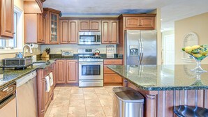 A kitchen with wooden cabinets, stainless steel appliances, granite countertops, and a trash can. - Lakefront Home in Barnstead w/ Seasonal Hot Tub (Barnstead)