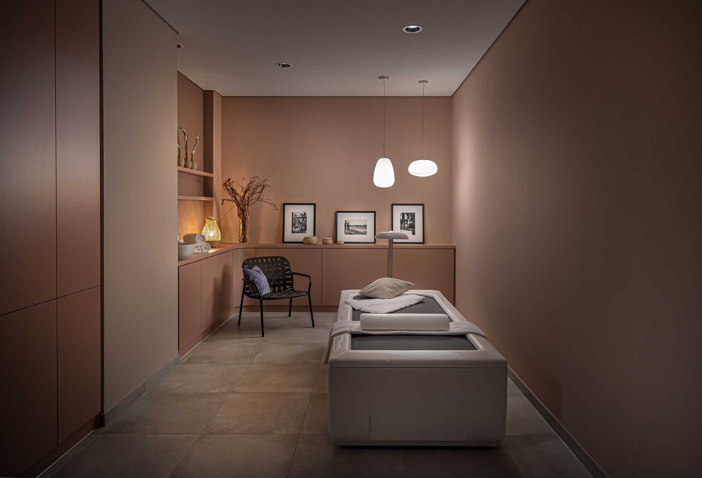 Ein moderner Wellnessraum mit Massagetisch, einem Sessel und gerahmten Bildern an der Wand.