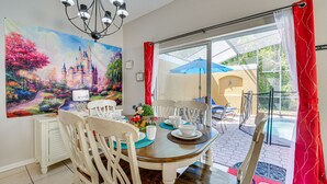 Ein Essbereich mit Tisch für vier Personen, weißen Stühlen, einer Kronleuchter und einem großen Gemälde mit Schlossmotiv an der Wand.