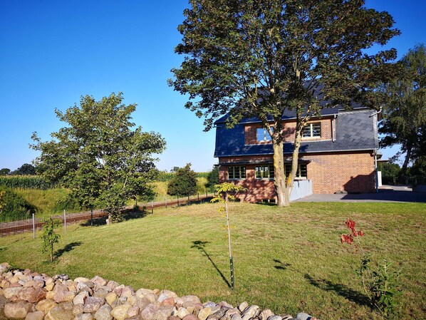 A two-story brick house with a dark roof, surrounded by a well-maintained lawn and a stone wall.