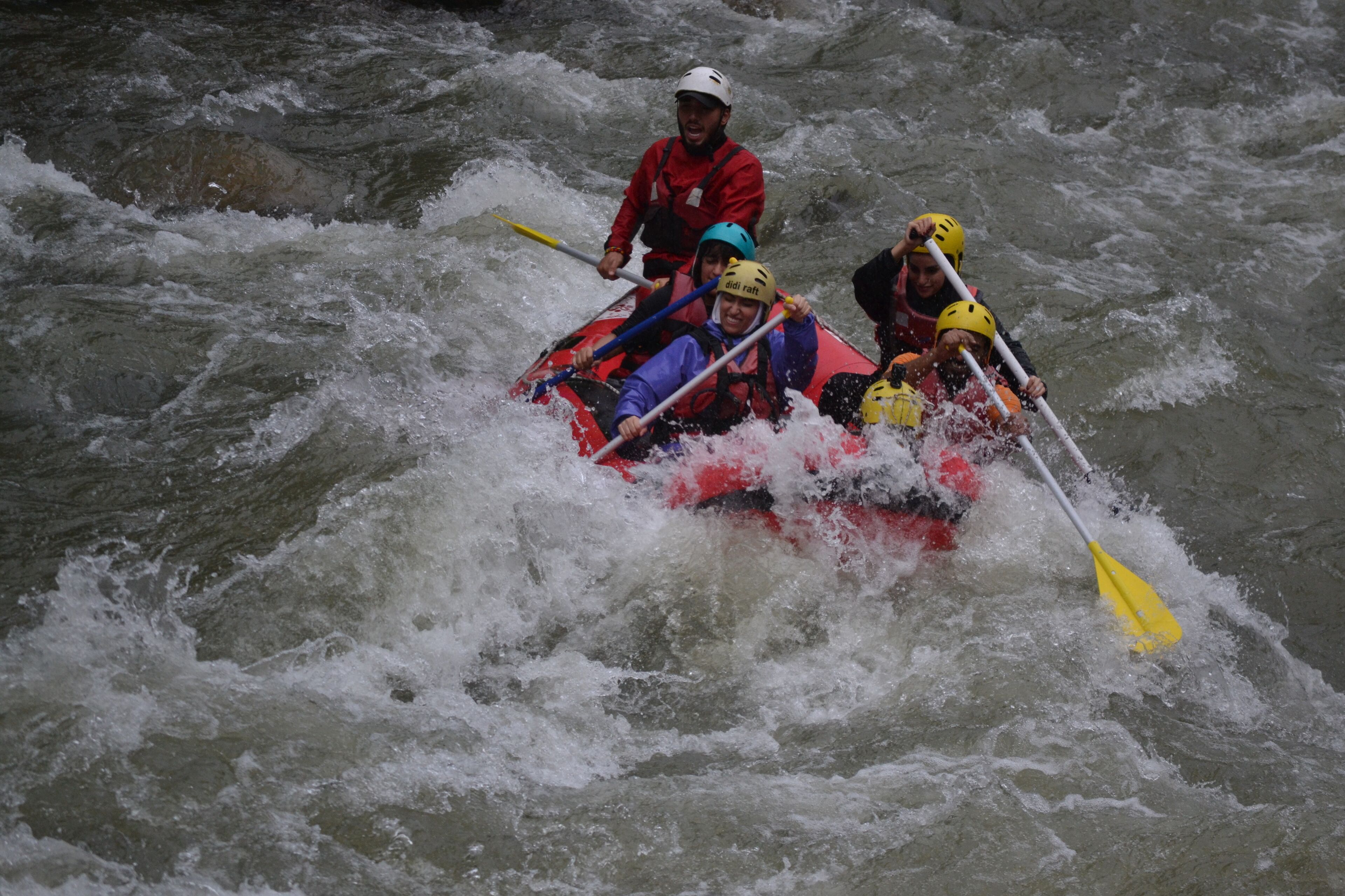 A group of people in a red raft navigating through a river with white water.