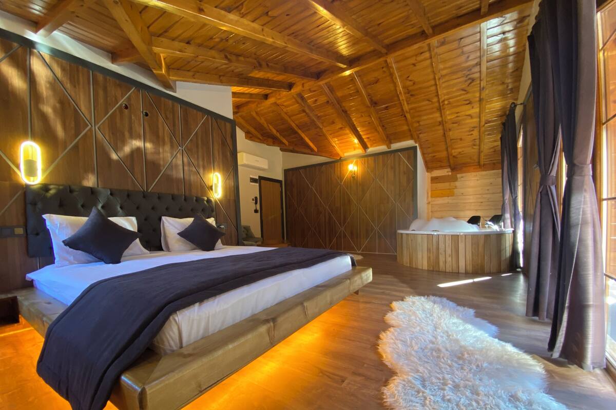 A spacious bedroom with a large bed, a wooden ceiling, and a hot tub in the corner.