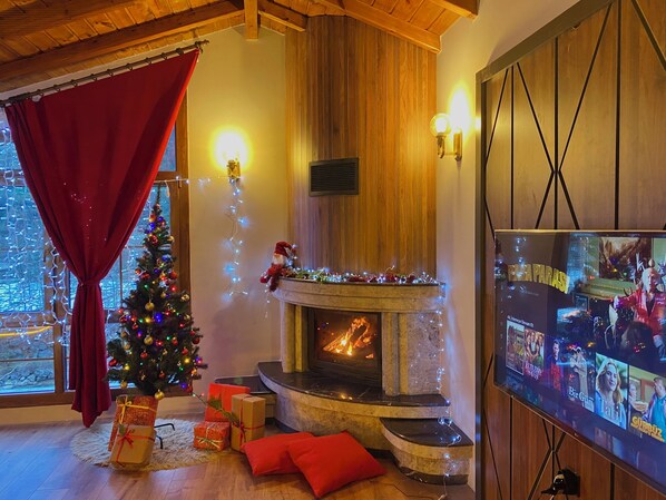 Ein gemütliches Wohnzimmer mit Kamin, Weihnachtsbaum und einem Fernseher, der Filmplakate zeigt.