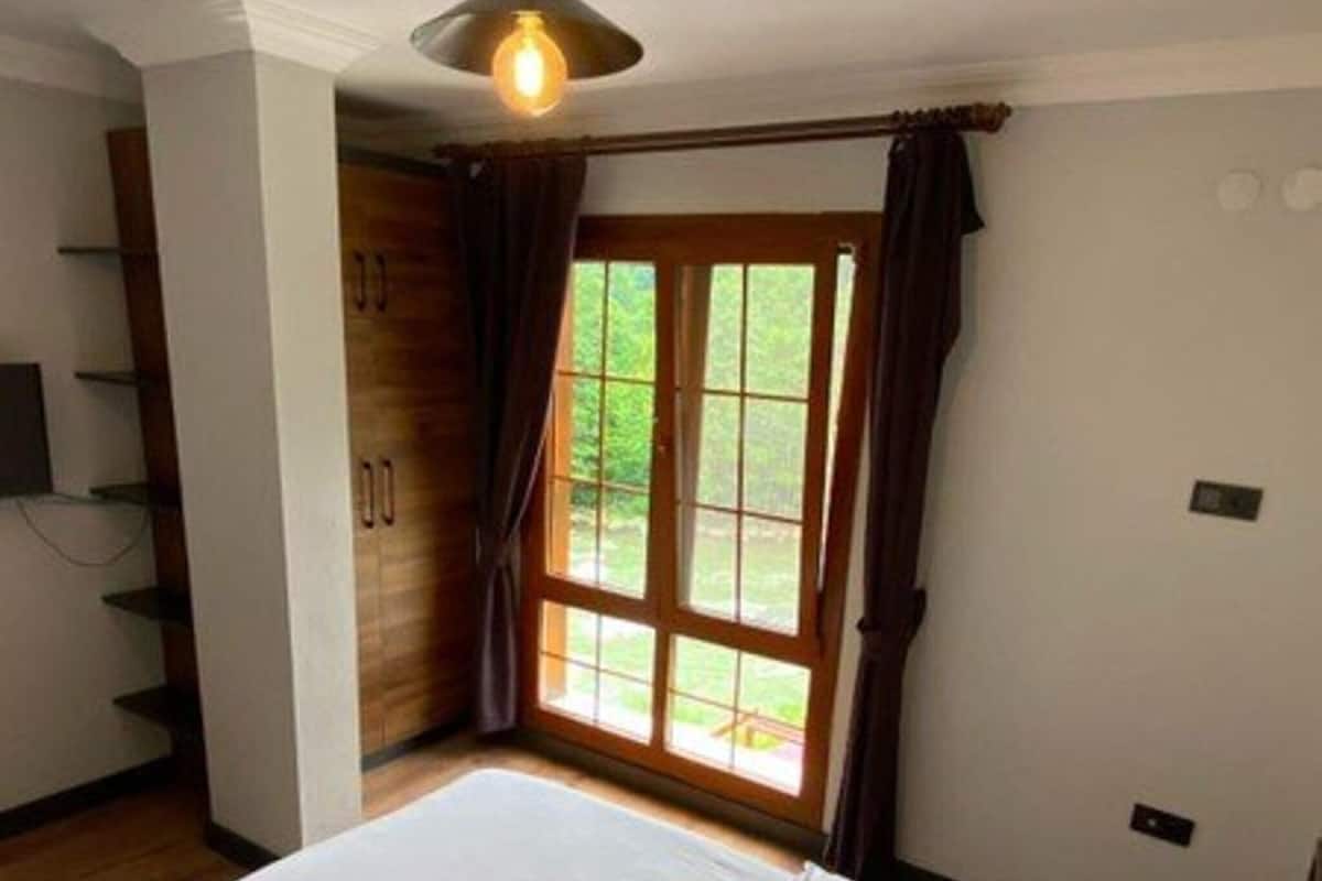 A bedroom with a large bed, a ceiling light, a window with curtains, and a wooden wardrobe.