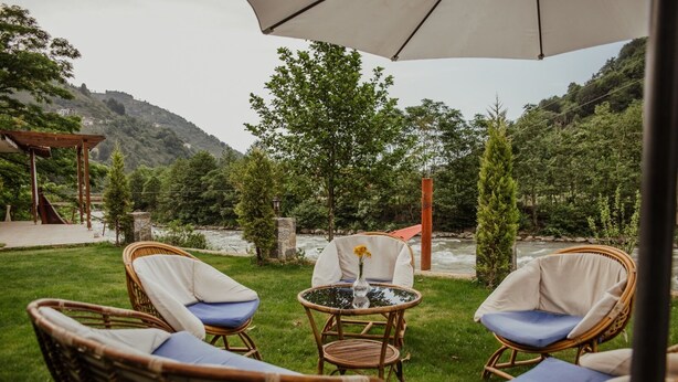 An outdoor seating area with wicker chairs and a table, overlooking a river and greenery.