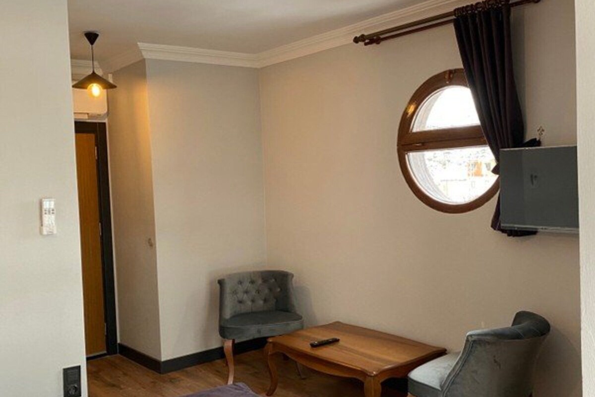 Un dormitorio con una cama, un ventanal redondo, una mesa, dos sillas y una lámpara colgante.