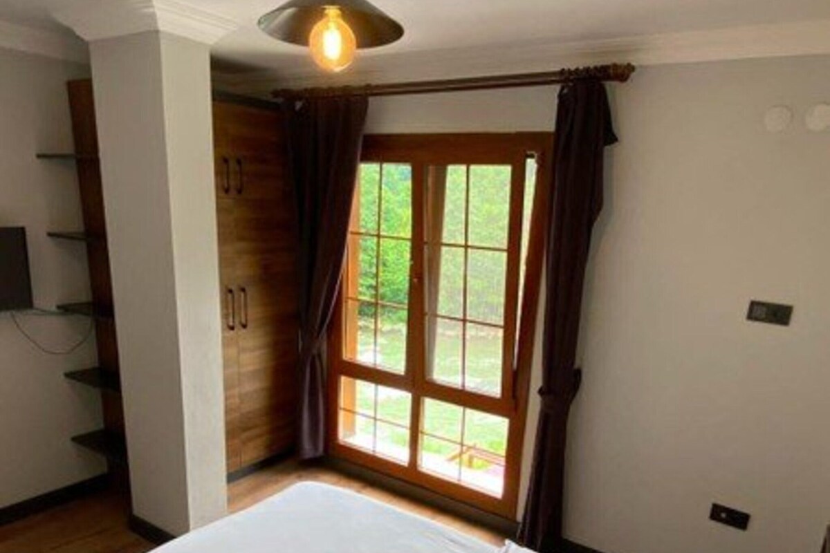 A bedroom with a large bed, a ceiling light, a window with curtains, and a wooden wardrobe.