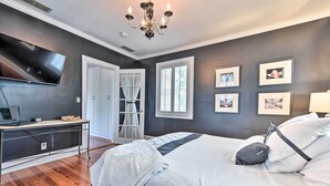 A bedroom with a bed, a desk, a TV, and a chandelier. - Historic Green Cove Springs Home - Walk to Coast! (Green Cove Springs)