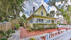 A yellow house with a white picket fence, surrounded by a garden with various plants and a brick pathway. - Historic Green Cove Springs Home - Walk to Coast! (Green Cove Springs)