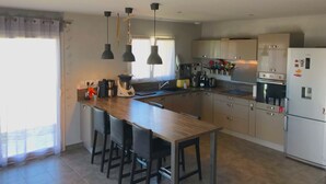 A modern kitchen with a central island, bar stools, pendant lighting, and stainless steel appliances.