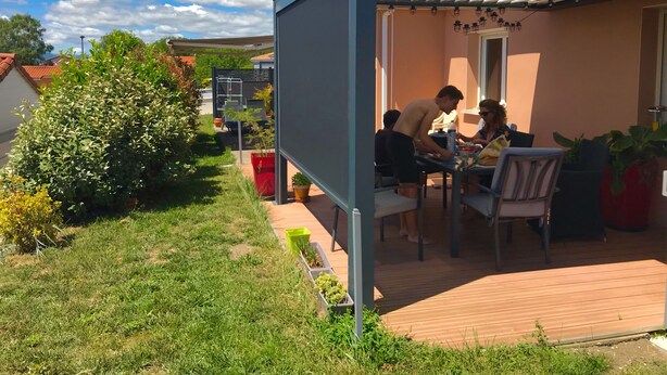 An outdoor patio with a table and chairs, surrounded by potted plants and a wooden deck.