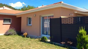 A single-story house with a red-tiled roof, a sliding glass door, and a dark-colored fence.