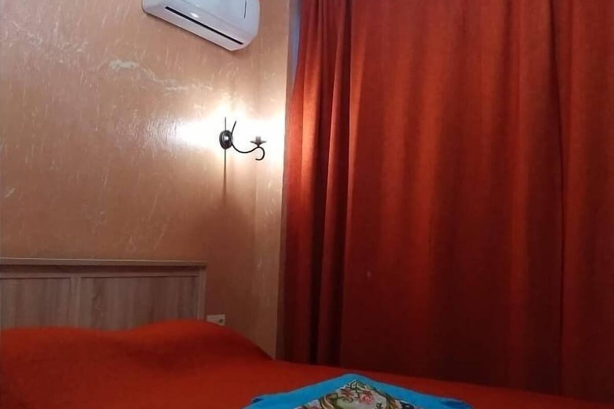 A room with a bed, an air conditioning unit, a wall-mounted light, and red curtains.