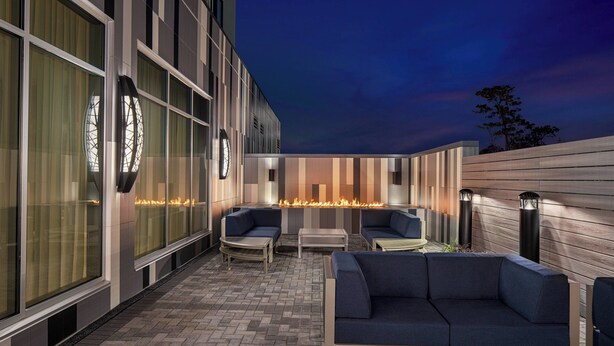 An outdoor seating area with a fire feature, modern furniture, and a view of the building's exterior. - Courtyard by Marriott Houston I-10 West/Memorial (Houston)