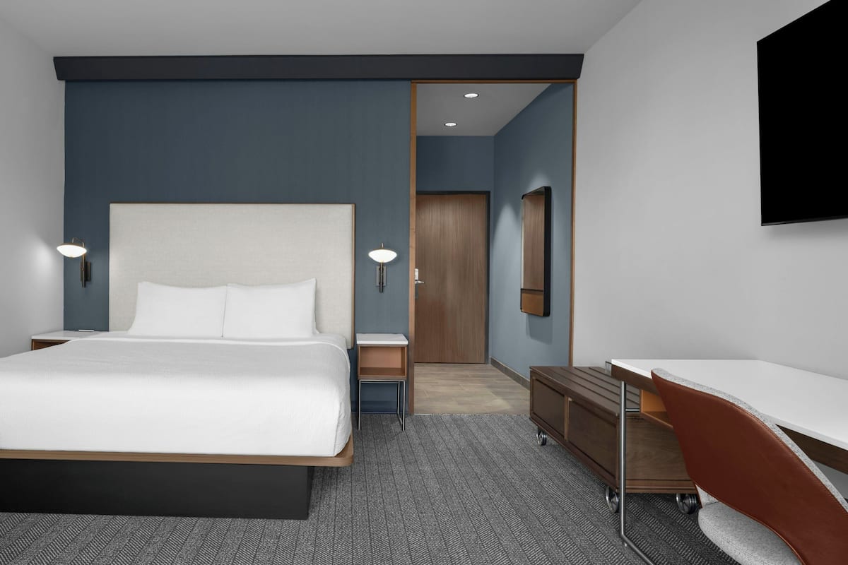 Une chambre d’hôtel moderne équipée d’un grand lit, de tables de chevet, d’un bureau et d’une armoire.