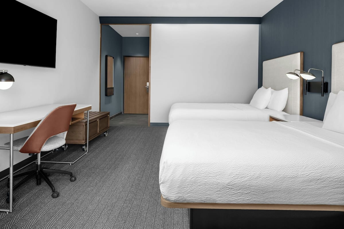 Une chambre d’hôtel moderne dotée d’un grand lit, d’un bureau avec une chaise, d’une télévision à écran plat et d’une table de chevet.