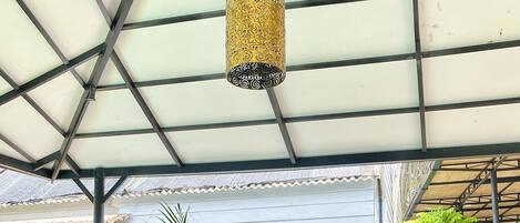 A covered outdoor bar area with a glass table, two bottles of Bintang beer, a bowl of black beans, and a vase with marigold flowers.