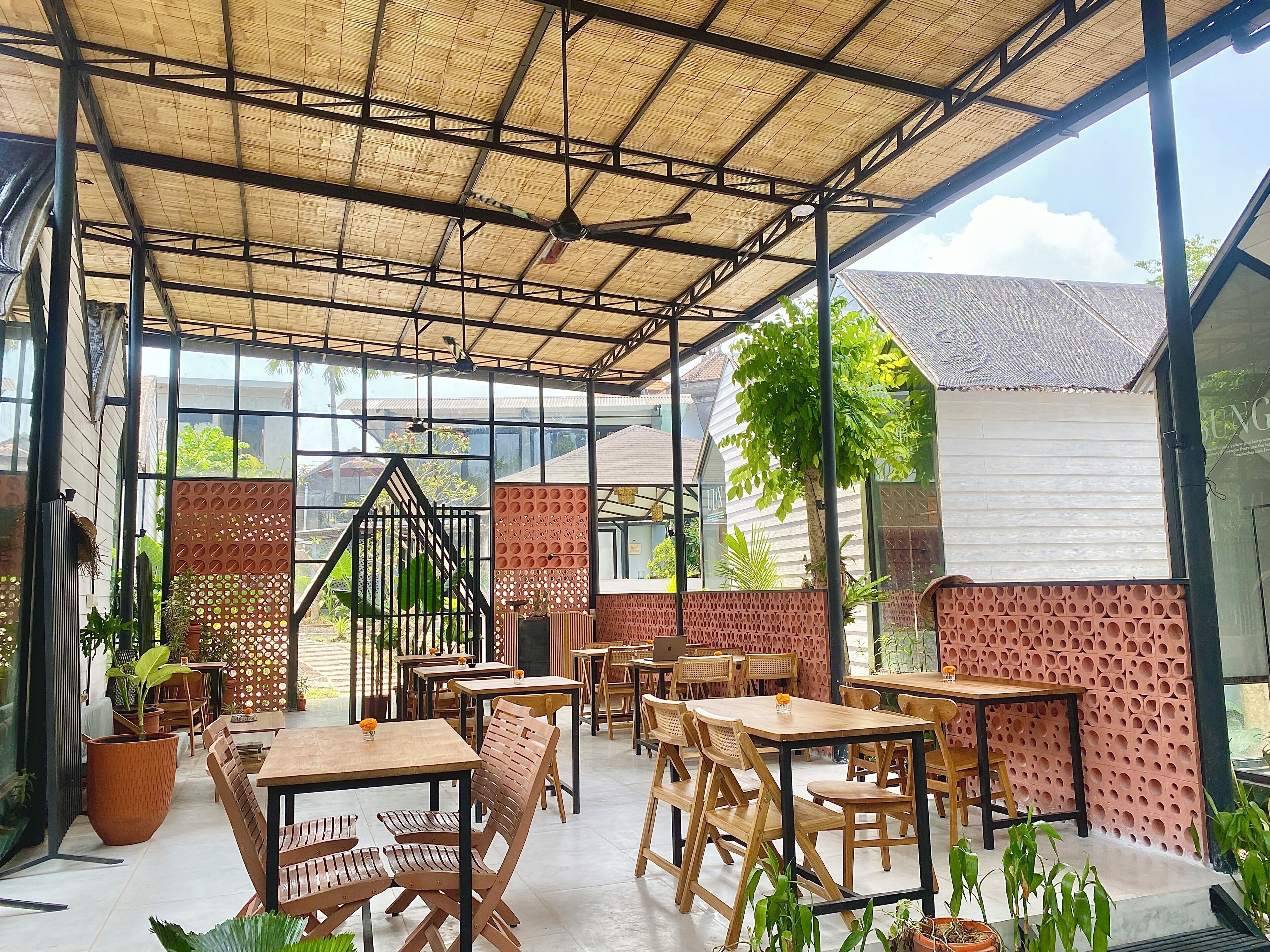 A covered outdoor seating area with tables and chairs, a ceiling fan, and potted plants.