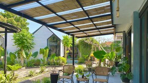 A covered patio area with outdoor seating and lush greenery. - The Jungle Hostel Canggu (Pererenan)