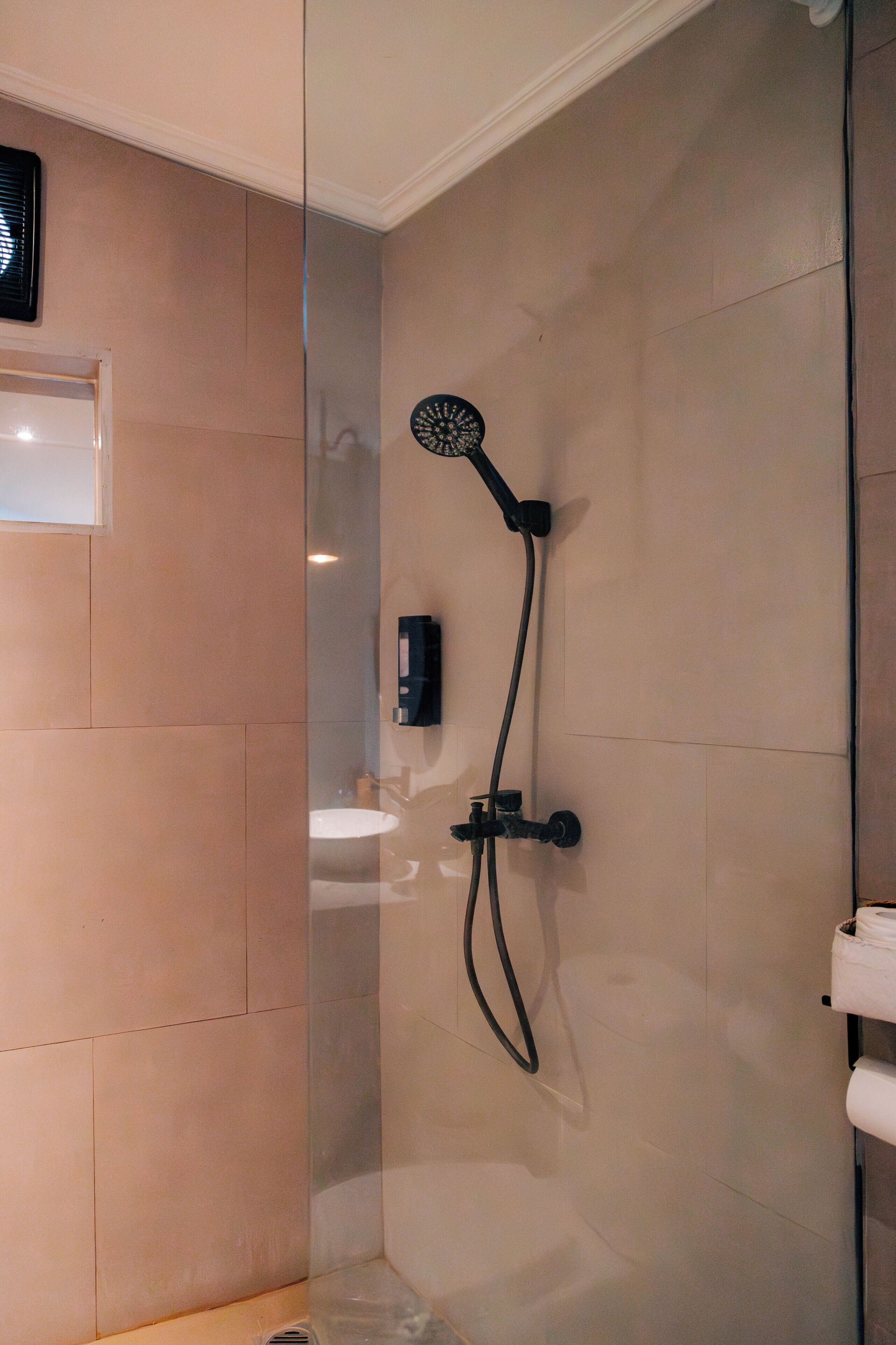 Un baño moderno con cabina de ducha de vidrio, ducha de mano y dispensador de jabón de pared.