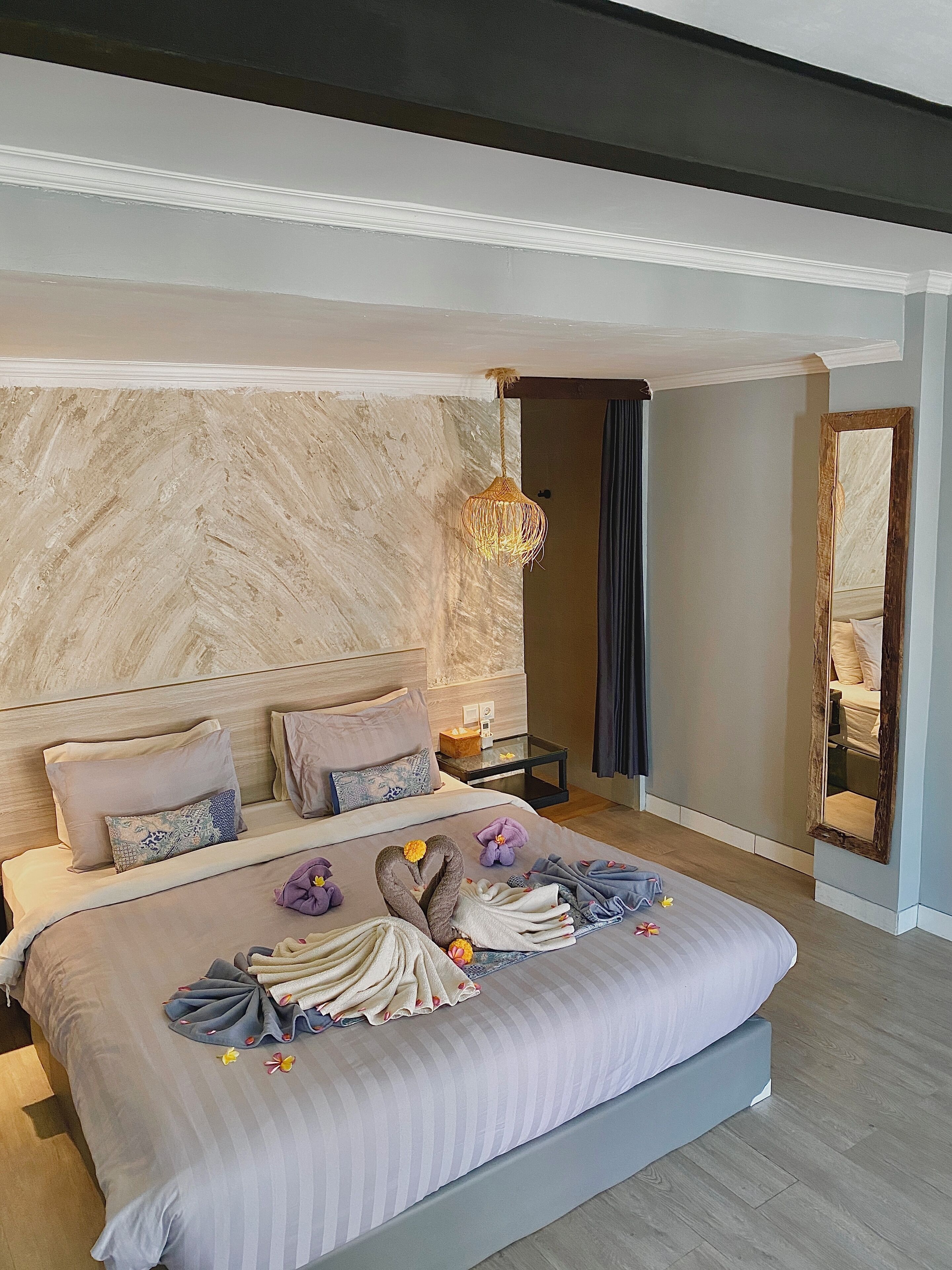 A modern bedroom with a large bed, a marble wall, a hanging light fixture, and a mirror.