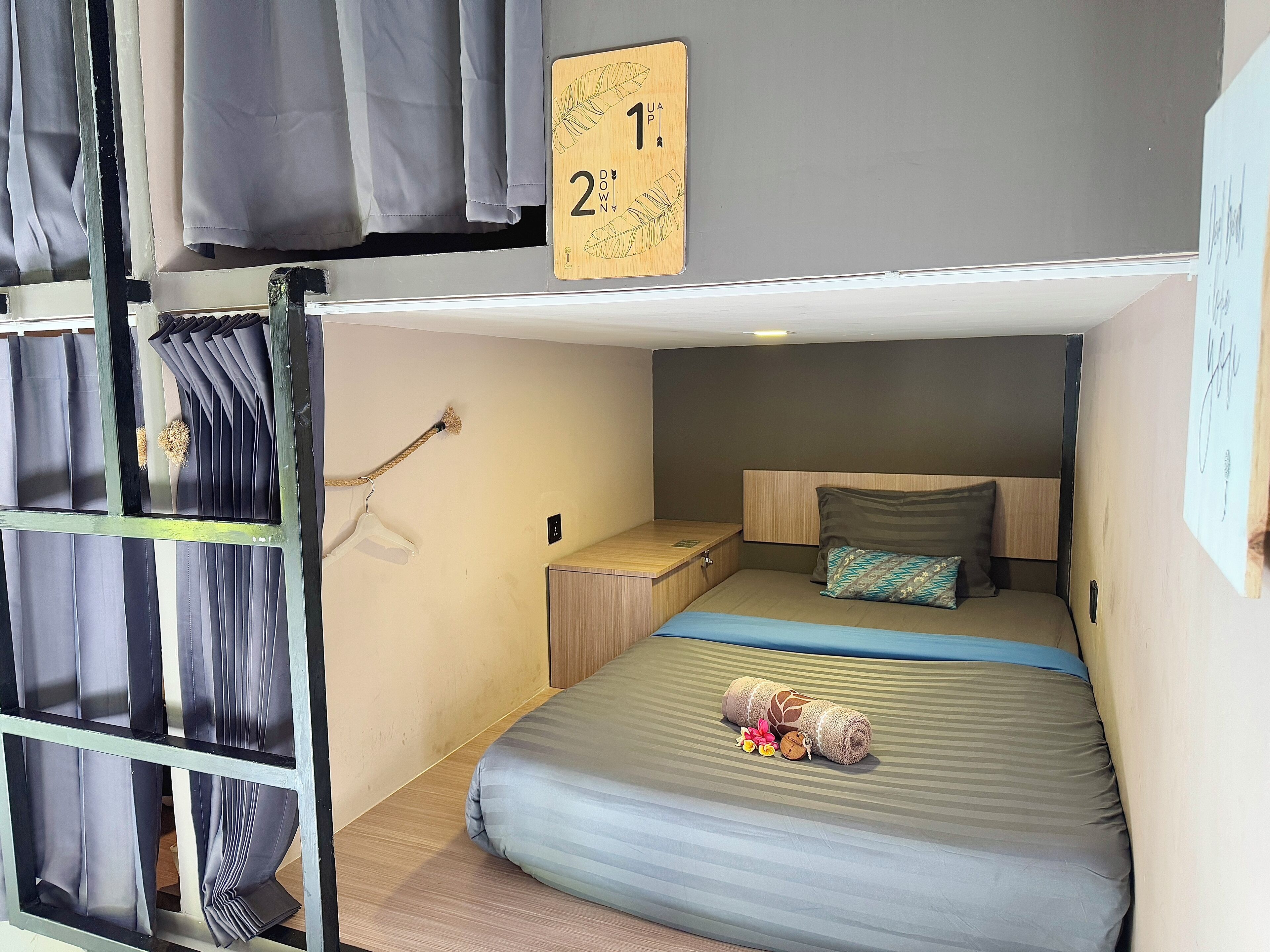 Habitación con literas, cabecero de madera, mesita de noche pequeña y cama con manta a rayas y una toalla enrollada.