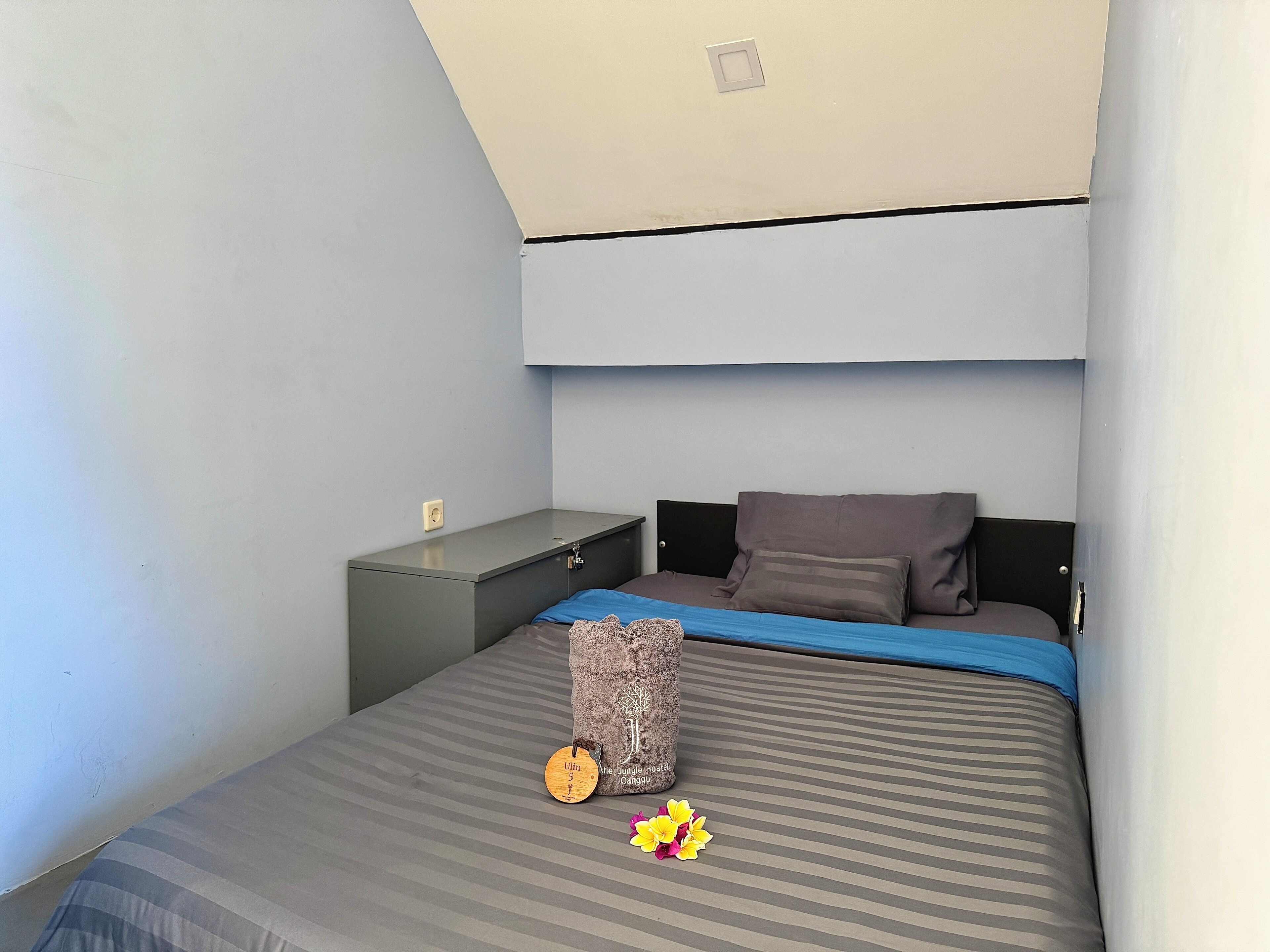 A bedroom with a bed, a nightstand, a storage unit, and a ceiling light.