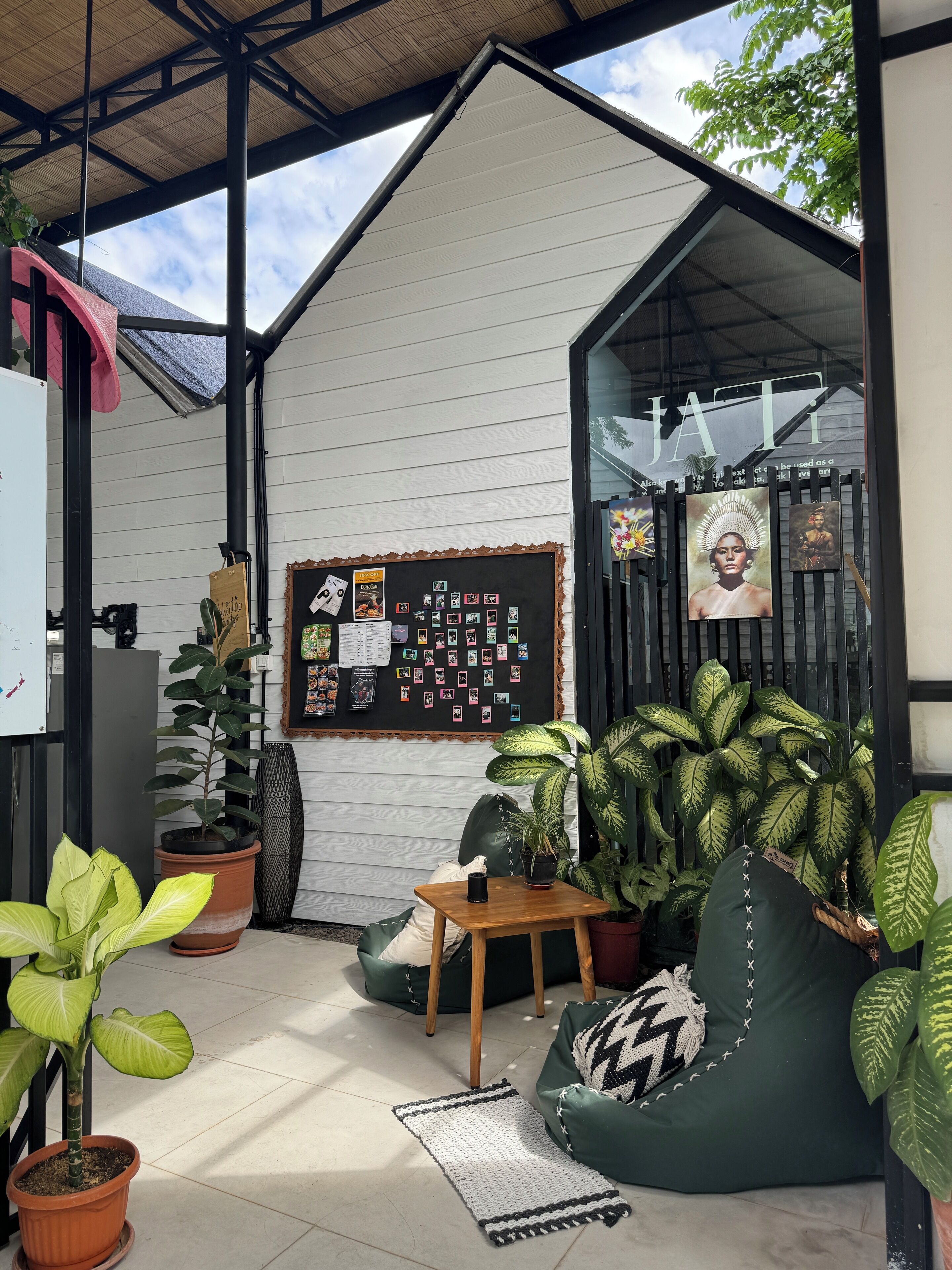 Una zona de estar al aire libre acogedora, con una mesa de madera, pufs de color verde y varias plantas en macetas.