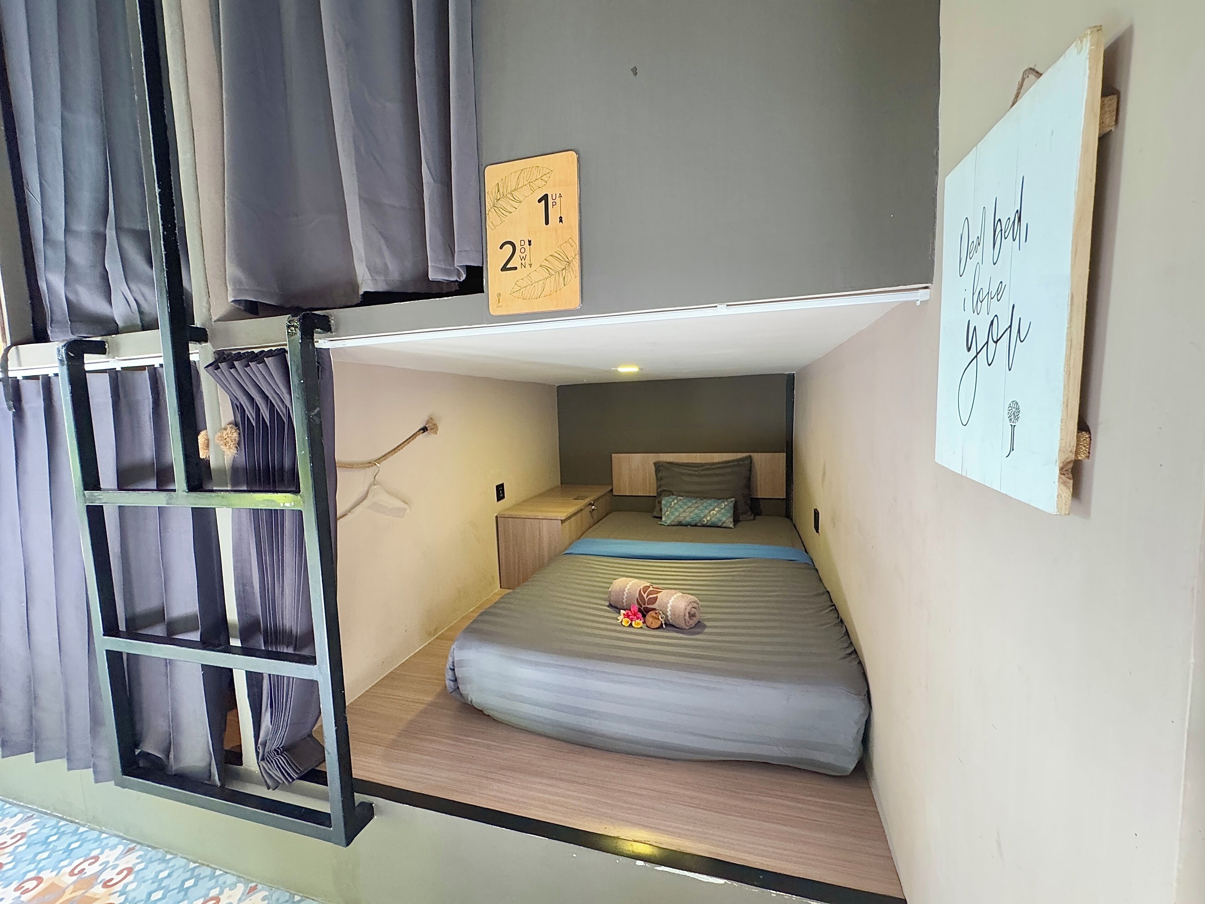 A bunk bed room with a ladder, a small bedside table, a pillow, and a sign with a flower illustration.