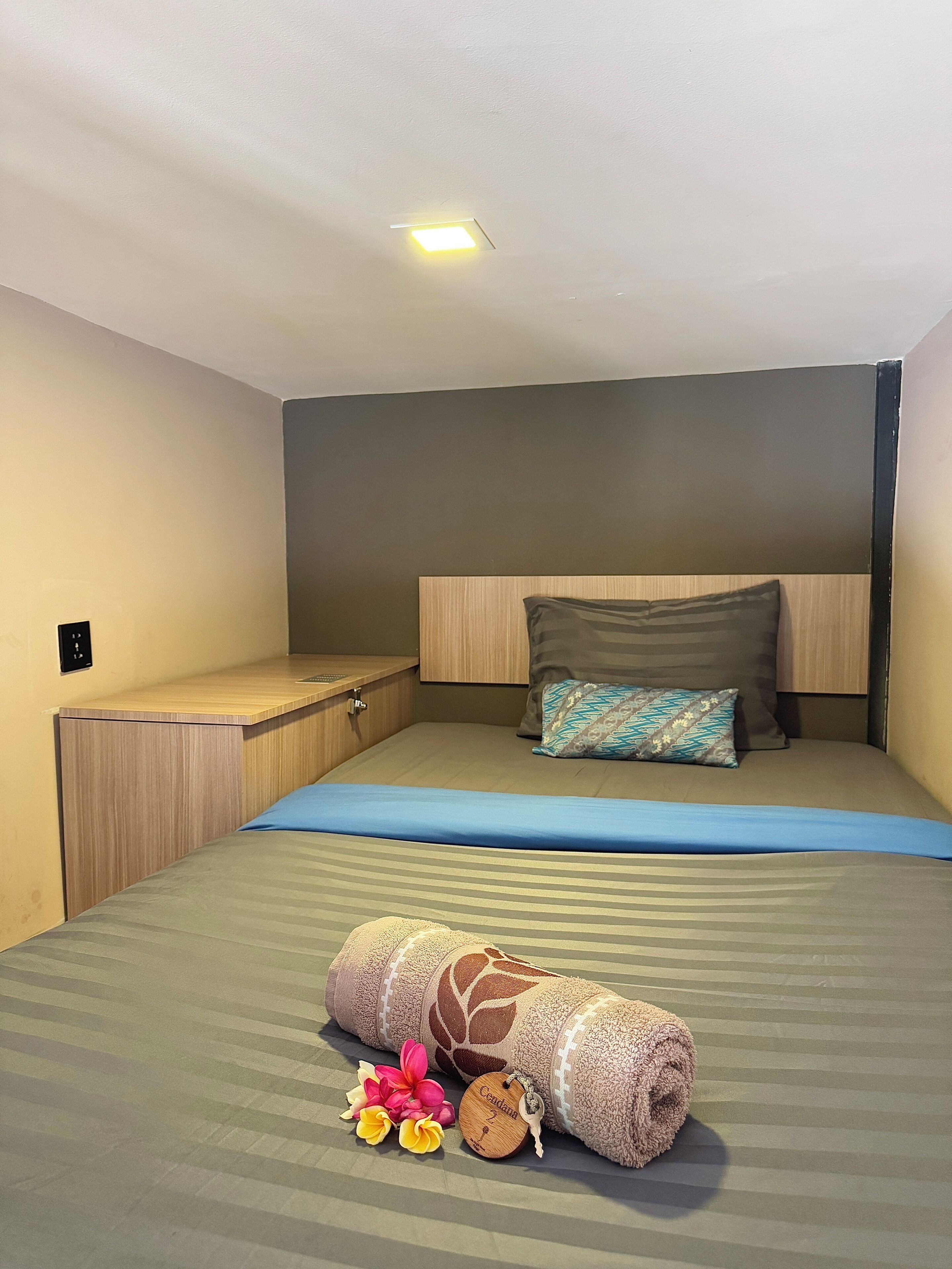 Una habitación de hotel compacta con una cama individual, un escritorio pequeño y una lámpara en el techo.