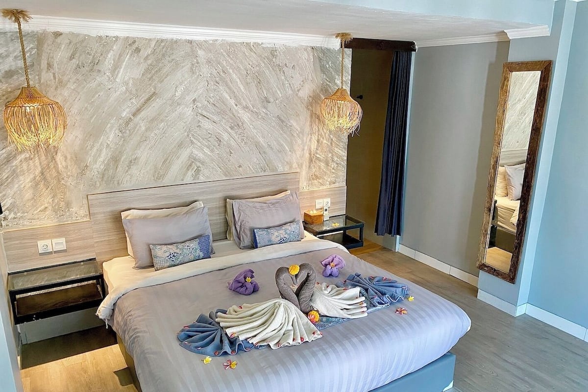 Un dormitorio moderno con cabecera de mármol, una cama grande con cubrecama a rayas, dos mesitas de noche y dos lámparas colgantes.