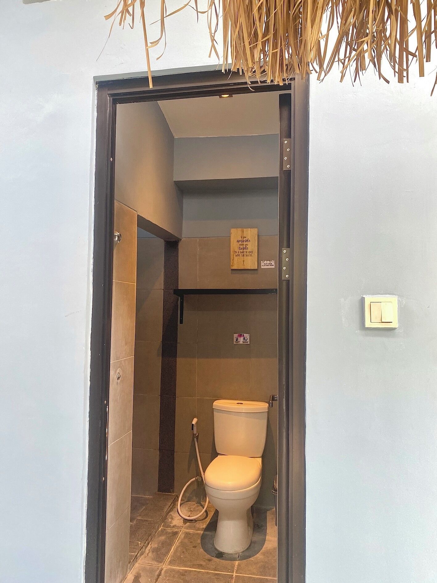 A small bathroom with a toilet, a shower area, and a sign on the wall.