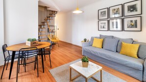 Una sala moderna con una mesa de comedor de madera, sillas negras, un sofá gris con cojines amarillos y una mesa de centro blanca, además de una escalera con barandilla de madera.