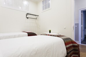 Hotellihuone, jossa on kaksi sänkyä, pieni pöytä, jossa on kasvi, ja ikkuna, jossa on verho.