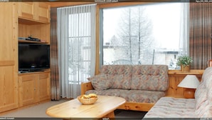 Kodikas olohuone, jossa on sohva, televisio ja ikkuna, josta avautuu näkymä puita kohti.