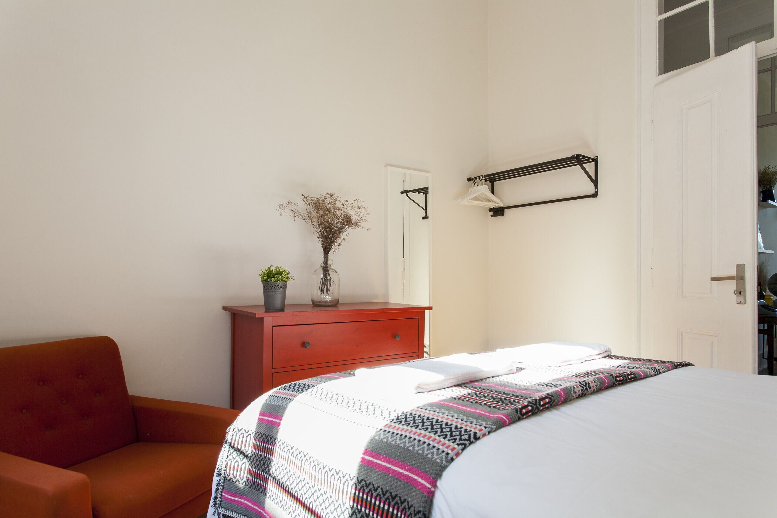 Une chambre à coucher avec un lit, une commode, une chaise rouge et une étagère fixée au mur.