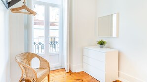 Ein Zimmer mit einem Korbstuhl, einem weißen Schminktisch, einem Spiegel und einer Topfpflanze.
