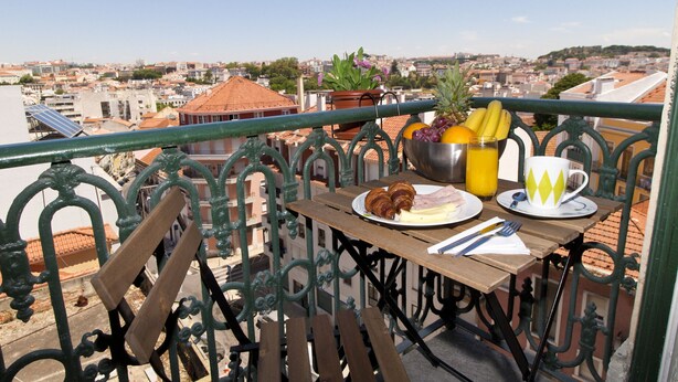 Ein Balkon mit einem Tisch, gedeckt für das Frühstück, mit Croissants, Obst und einer Tasse.