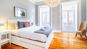 Ein Schlafzimmer mit Bett, Sessel, Nachttisch, einer Lüster und einem Fenster mit Blick.
