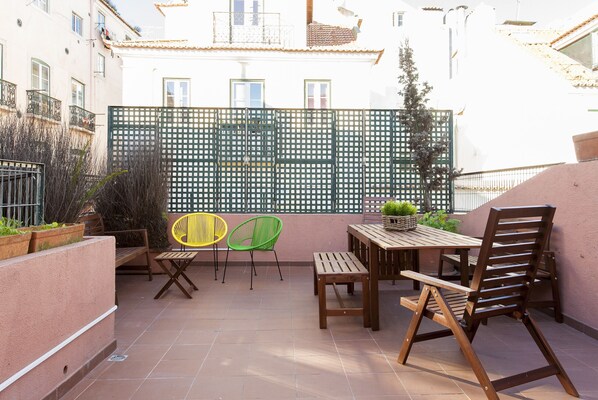 Un patio con una mesa y sillas de madera, un cerco de malla verde y plantas en macetas.