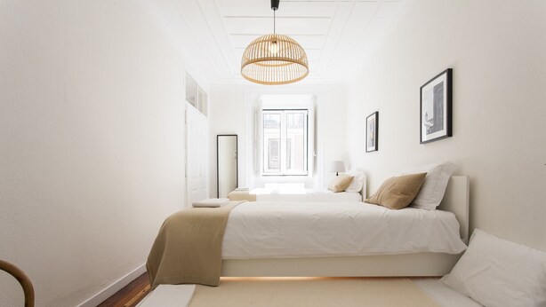 Un dormitorio minimalista con una cama grande, una mesita de noche, una silla y una lámpara colgante.