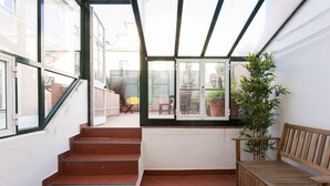 Una escalera conduce a un espacio exterior techado con un banco de madera y una planta en maceta.
