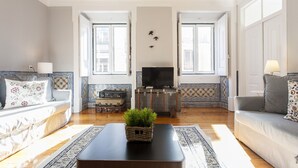 Una sala de estar con un sofá, una mesa de centro con una planta, un televisor y una pared con diseño.
