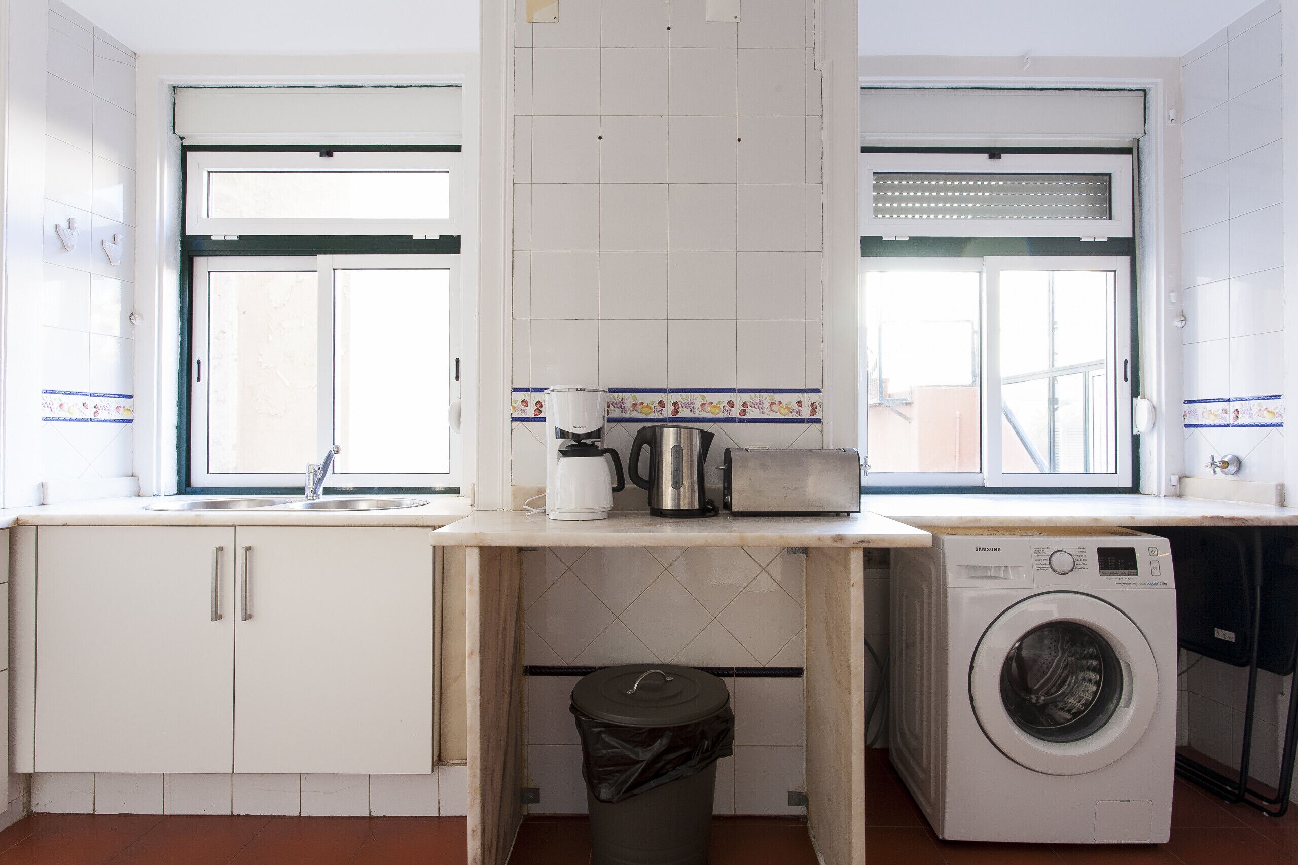 Une petite cuisine équipée d’un lave-linge, d’un évier et d’une fenêtre.